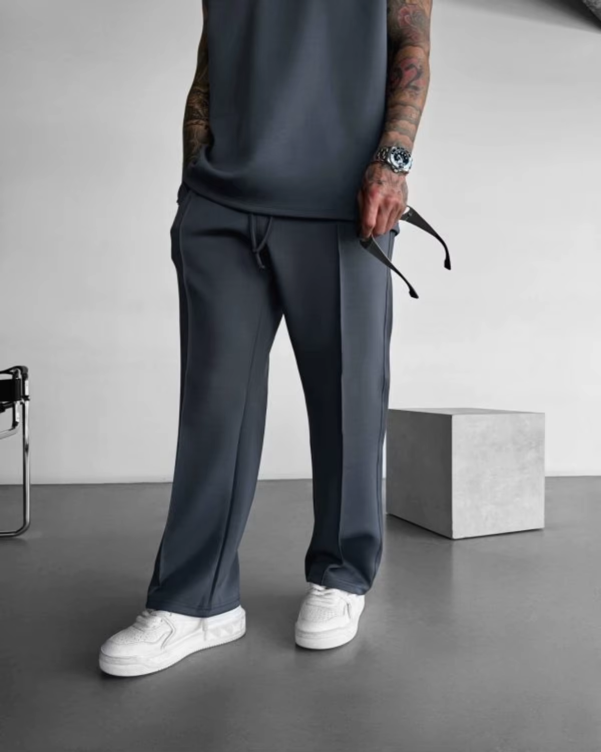 Person in dark gray joggers and white sneakers standing in a minimalist studio.