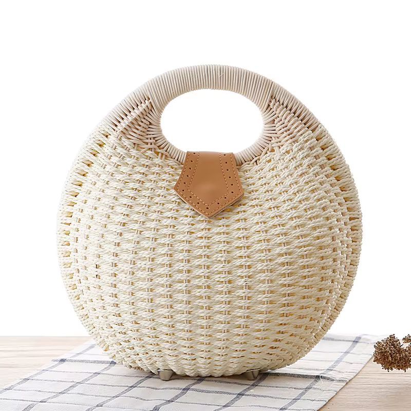 Round woven wicker bag with a tan leather accent, standing on a tiled floor