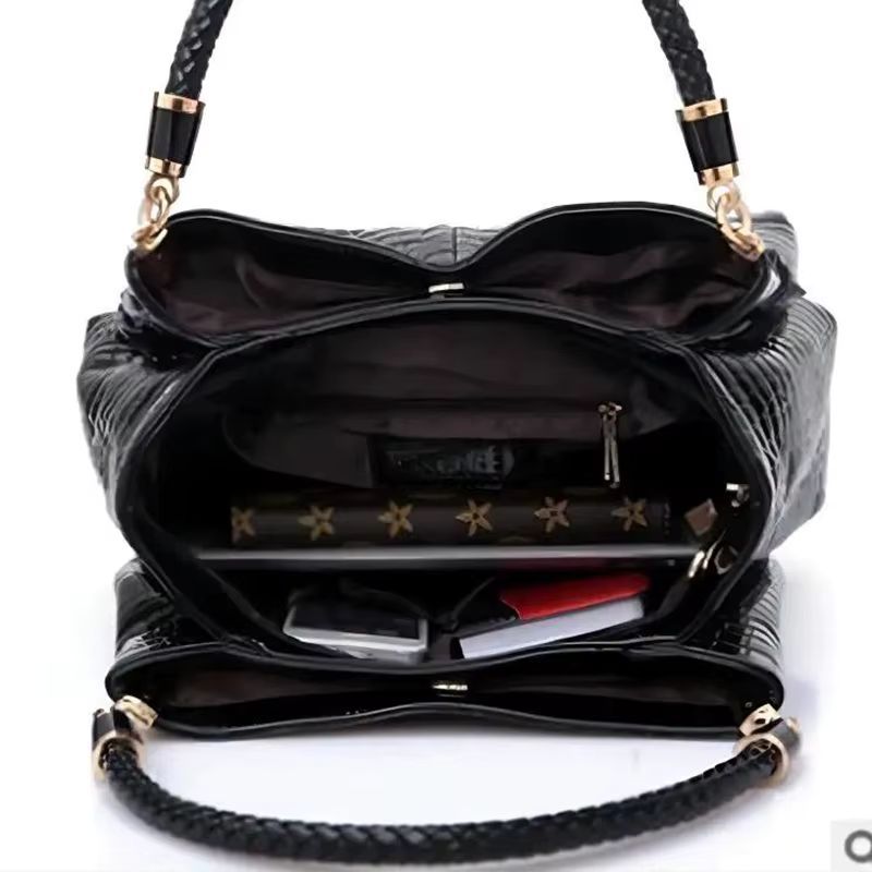 Black crocodile-texture handbag with braided handles and gold hardware on a plain background