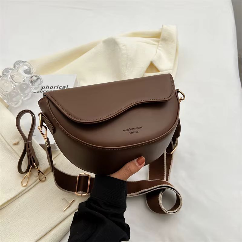 Brown leather crossbody purse with strap and cream tote bag on a white bed.