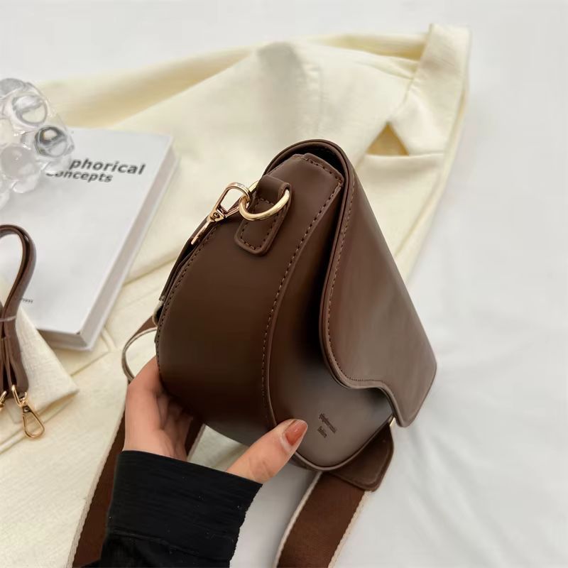 Brown leather crossbody purse with strap and cream tote bag on a white bed.