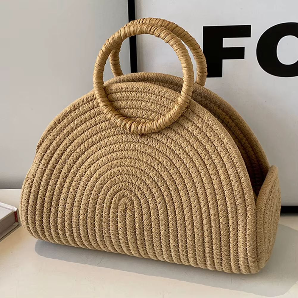 Straw woven handbag on a table beside yellow tulips, with a black leather sofa in the background