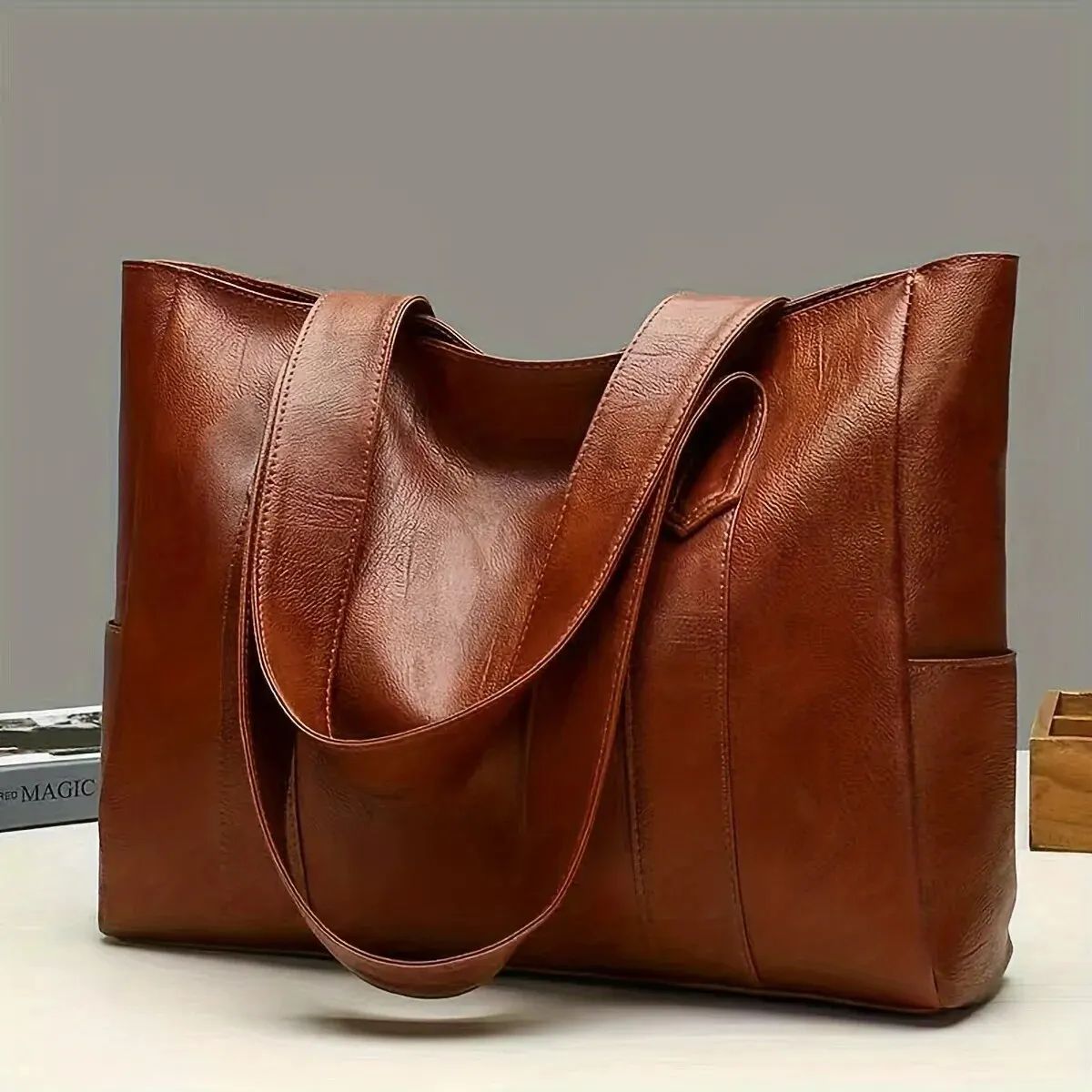 Brown leather tote bag with shoulder straps on a plain background