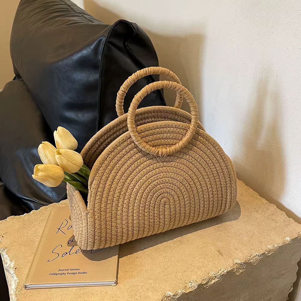 Straw woven handbag on a table beside yellow tulips, with a black leather sofa in the background