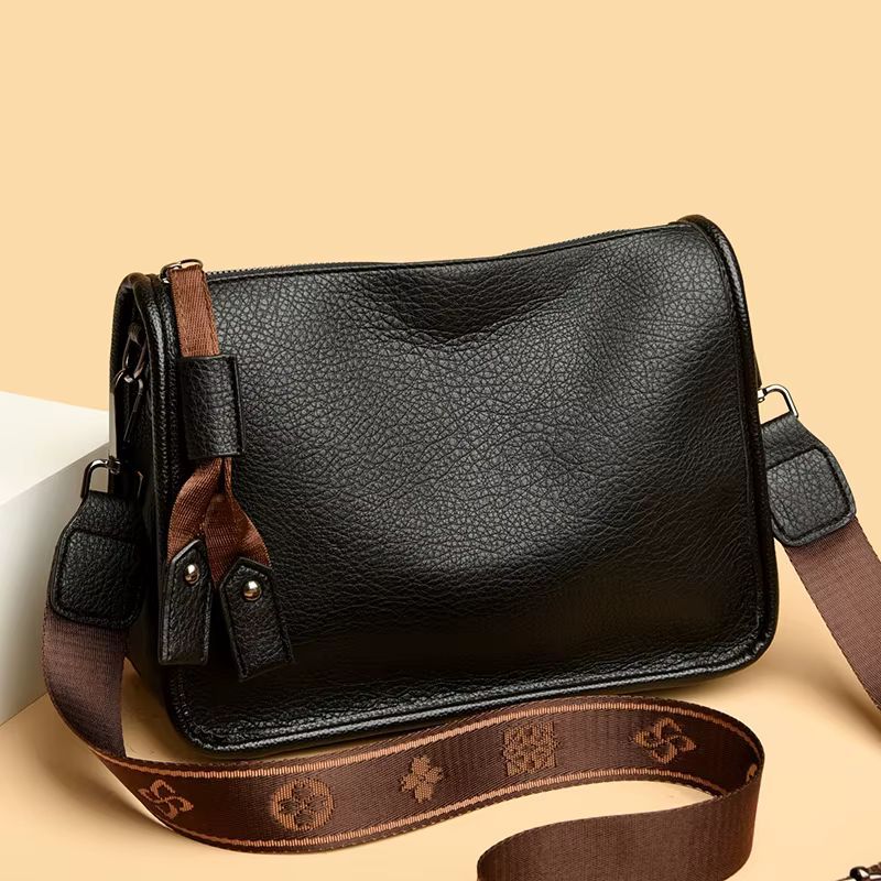 Black leather crossbody bag with brown patterned strap on a light background