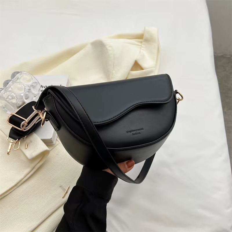 Black crossbody bag with gold hardware on a white bed, held by a gloved hand