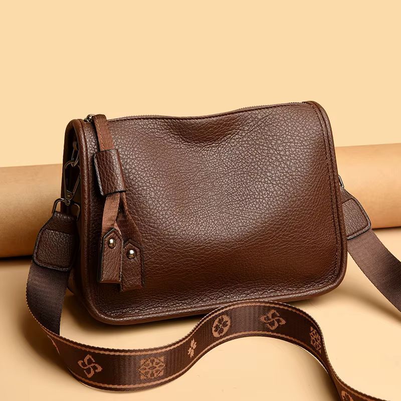 Black leather crossbody bag with brown patterned strap on a light background