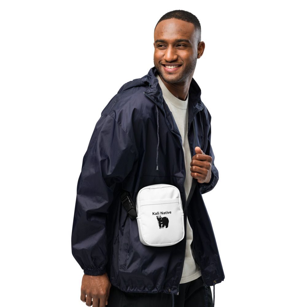Smiling man in a navy jacket carrying a white crossbody bag on a white background