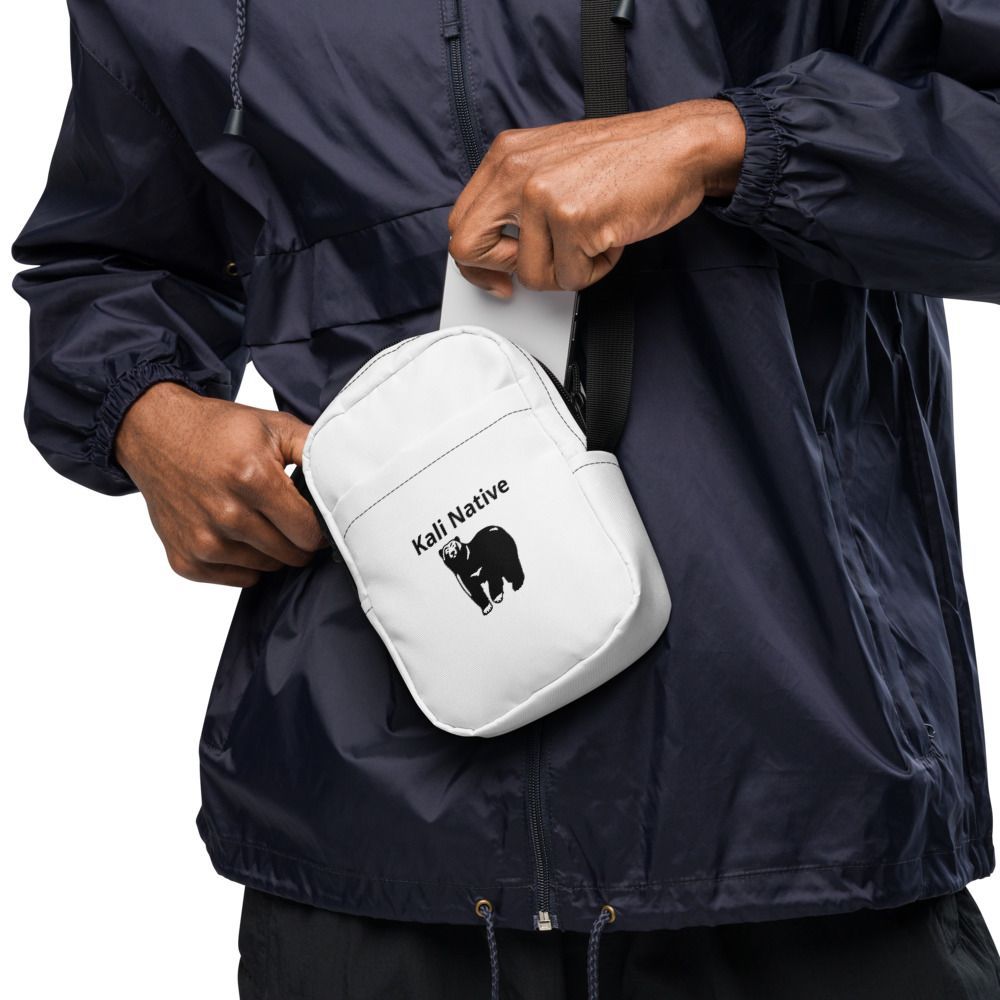 Smiling man in a navy jacket carrying a white crossbody bag on a white background