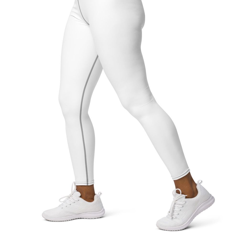 Woman in beige sports bra and white leggings posing in a sunlit studio with woven decor and textured floor