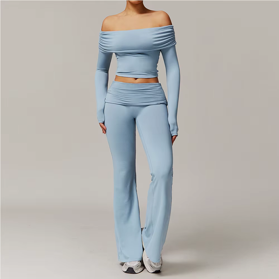 Person in light blue off-shoulder top and pants posing against a plain gray background