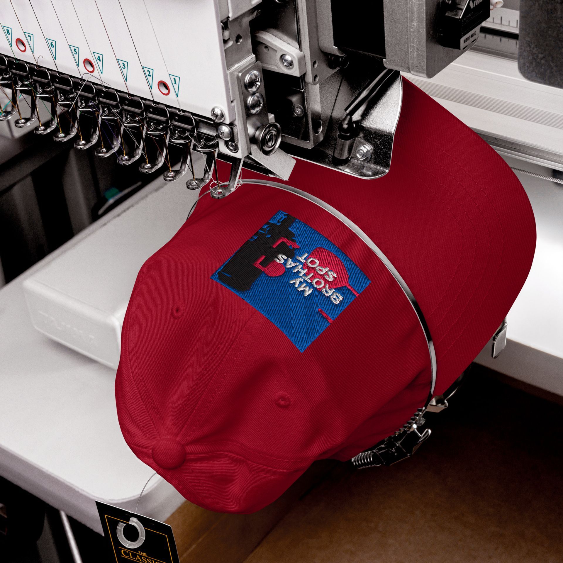 Red baseball cap with a colorful patch, resting on a dark cloth beside sunglasses.