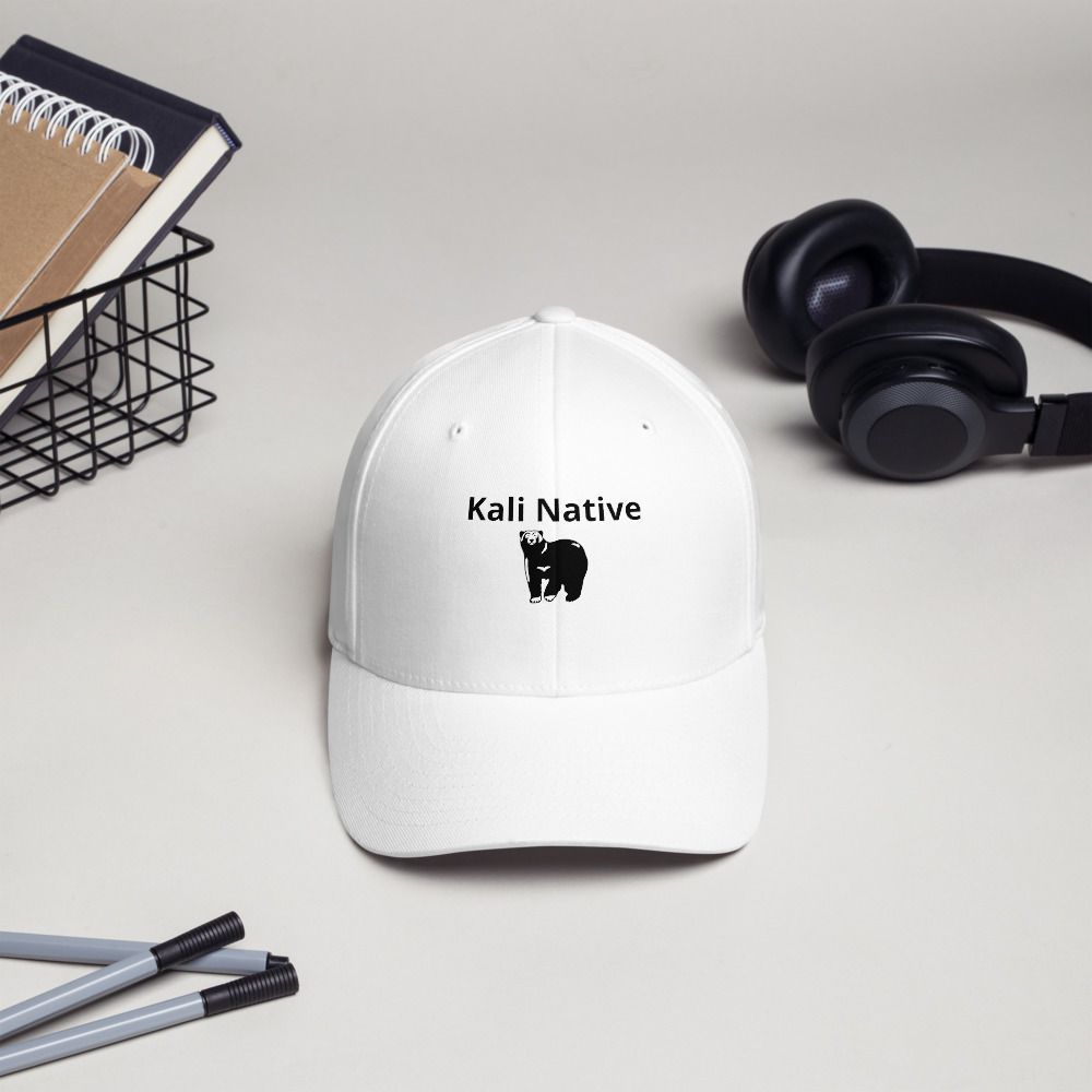 White cap with “Kali Native” logo, beside black headphones, pencils, and a notebook on a desk.