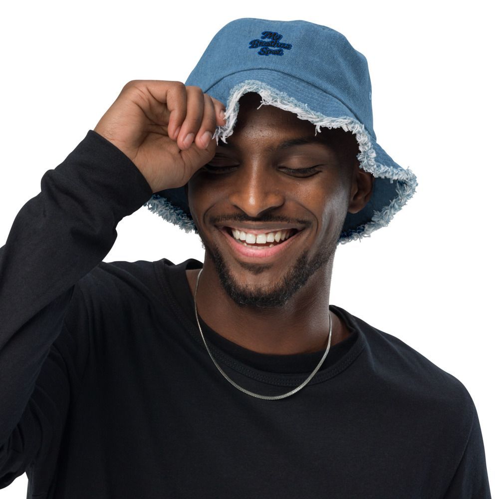 Smiling man in black shirt adjusting a blue bucket hat against a white background