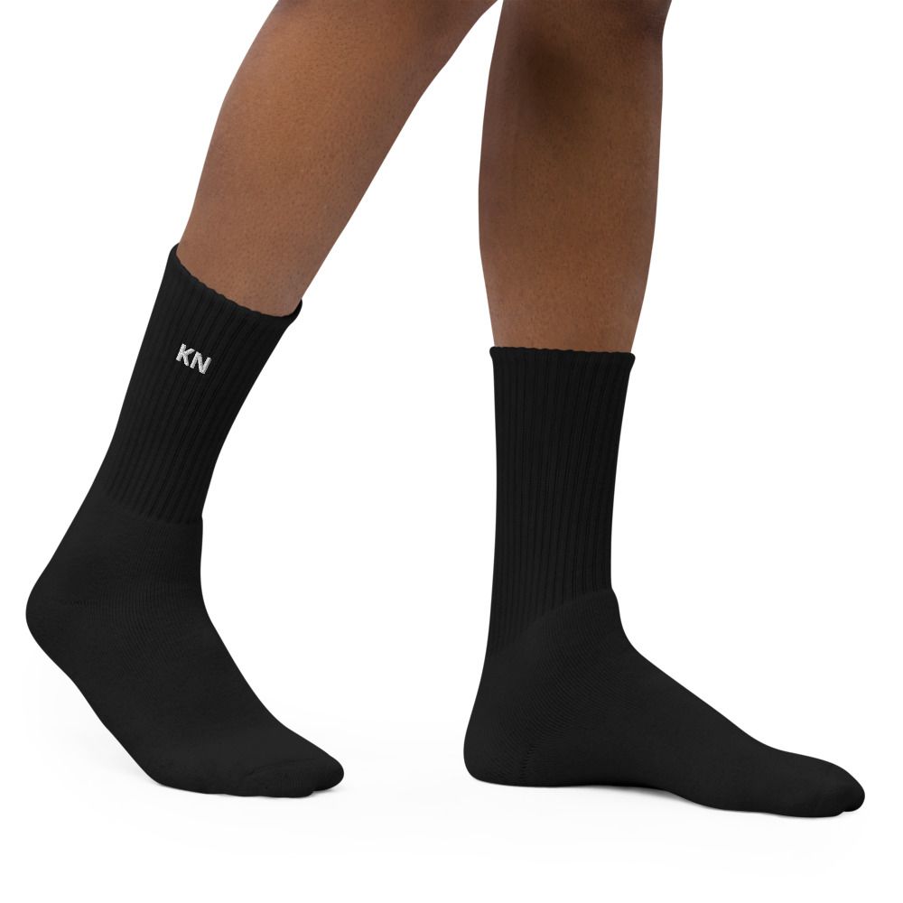 Black socks on a pair of crossed legs, one with a small white “KN” logo.
