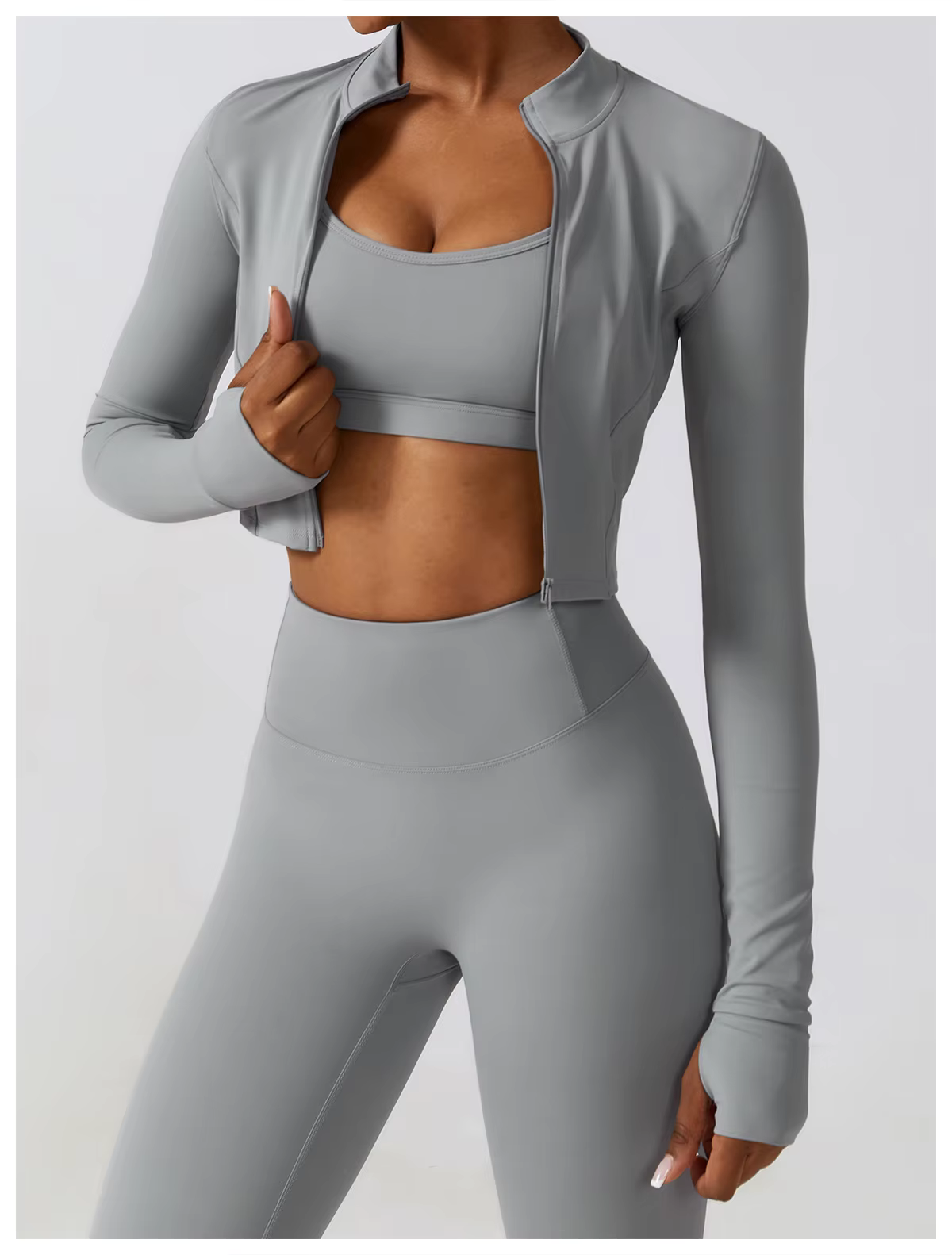 Gray athletic outfit with cropped jacket, sports bra, and leggings on a person against a white background