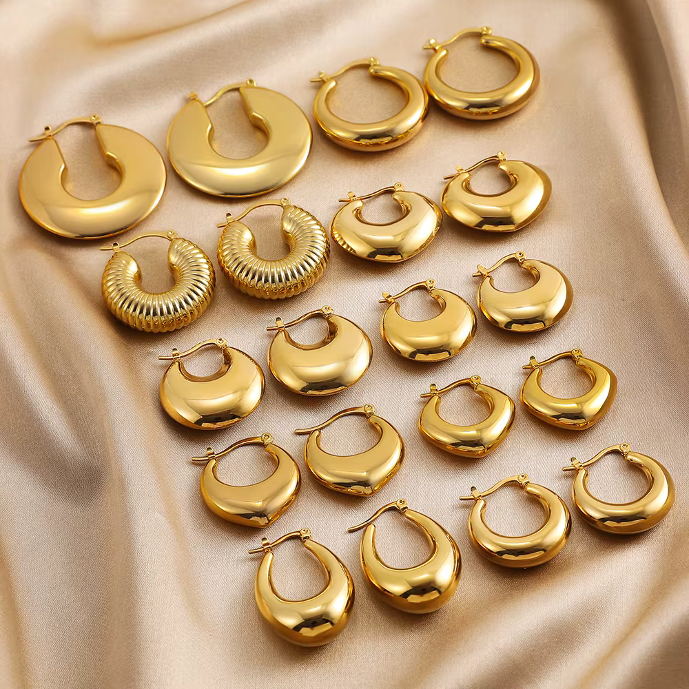 Gold hoop earrings arranged on beige satin fabric, showing assorted sizes and textured styles