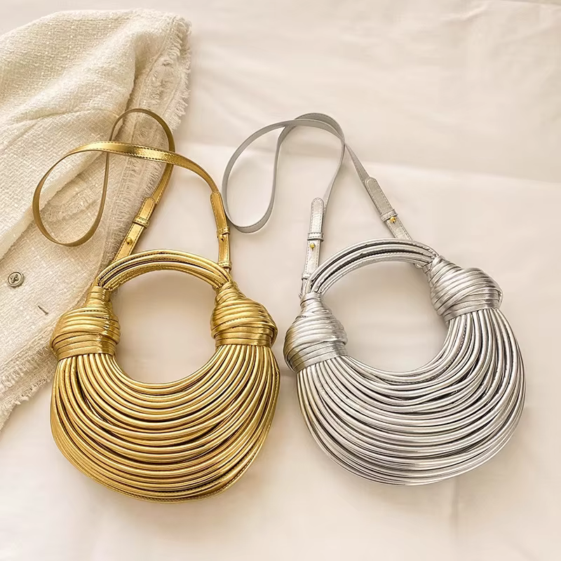 Two metallic layered crescent necklaces, one gold and one silver, on a light fabric background