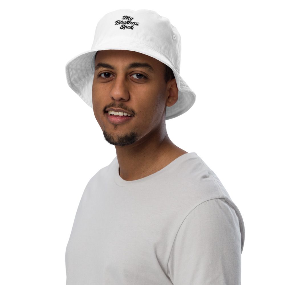Man wearing a white bucket hat and light gray shirt, smiling against a plain white background