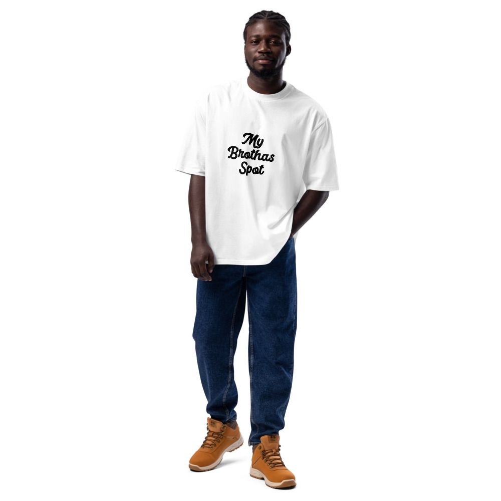 Man standing on a white background wearing a white graphic T-shirt, blue jeans, and tan boots.