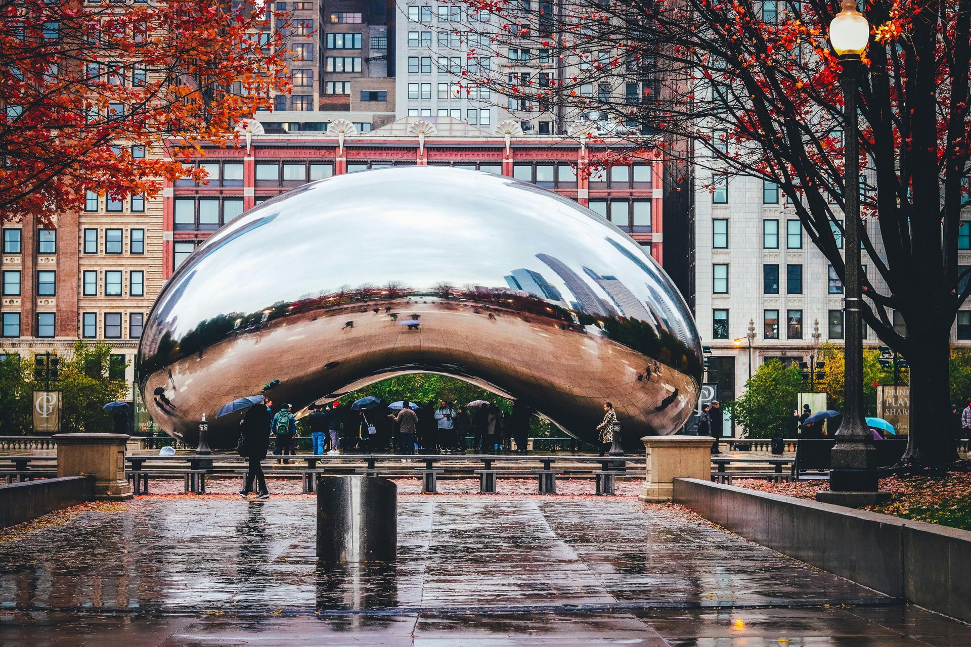 A large silver sculpture in a park with buildings in the background