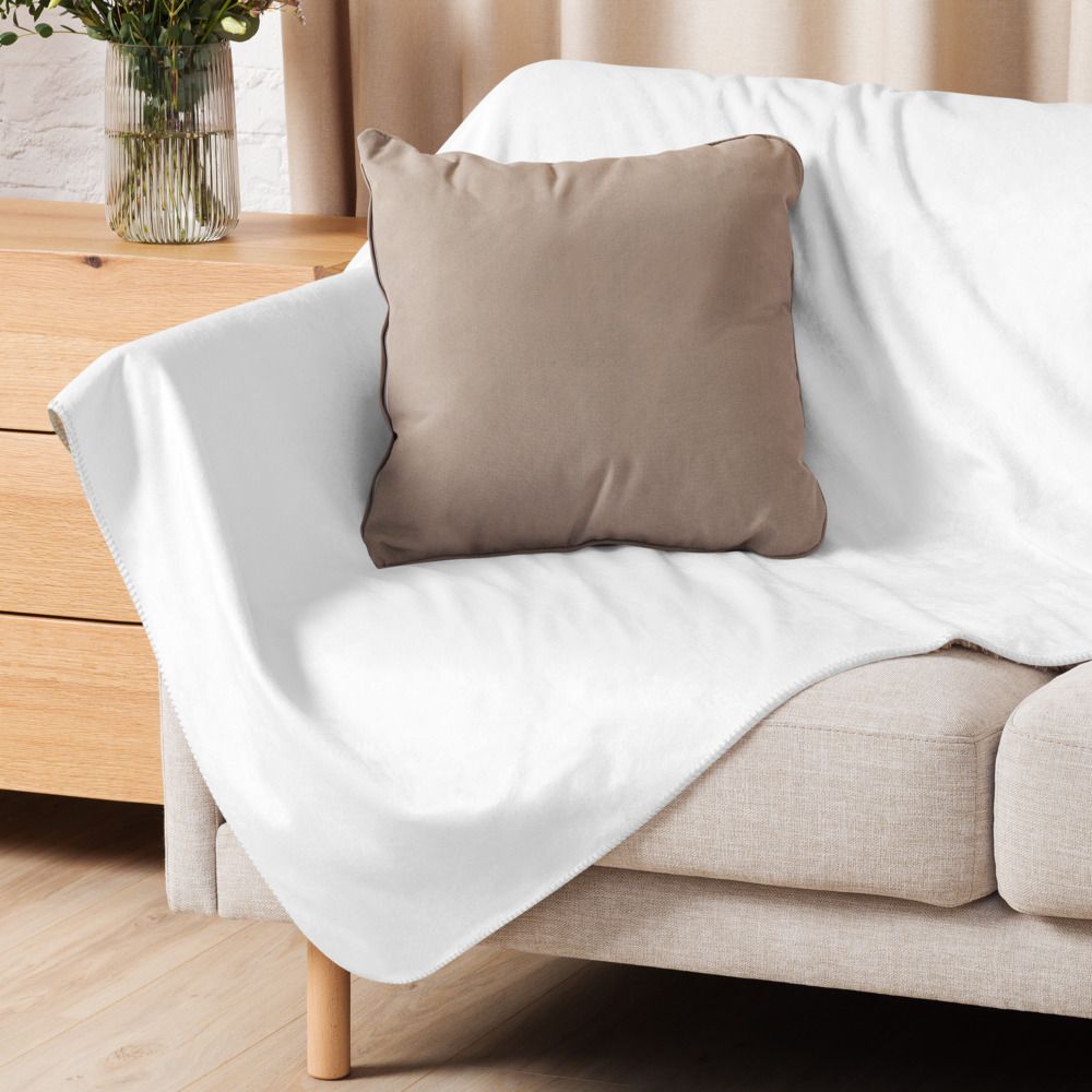 Smiling person wrapped in a white blanket on a couch beside a lit lamp