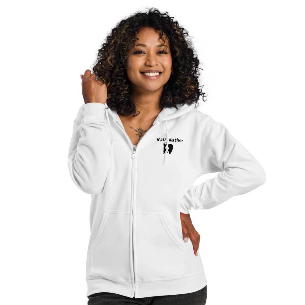 Smiling person in a white zip-up hoodie with one hand raised and one on hip