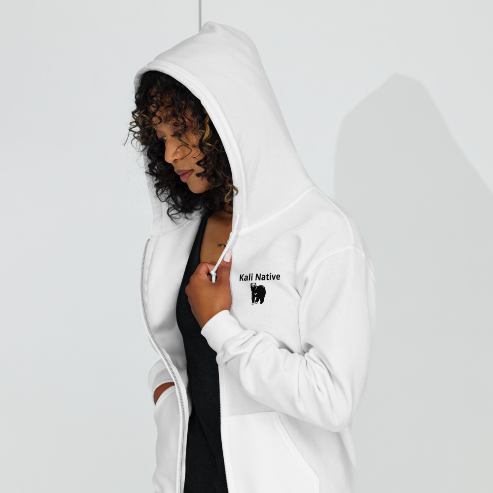 Smiling person in a white zip-up hoodie with one hand raised and one on hip