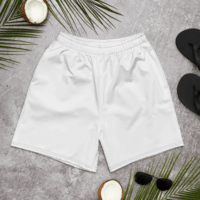 White athletic shorts laid flat on a gray surface with sunglasses, coconut halves, and palm leaves nearby