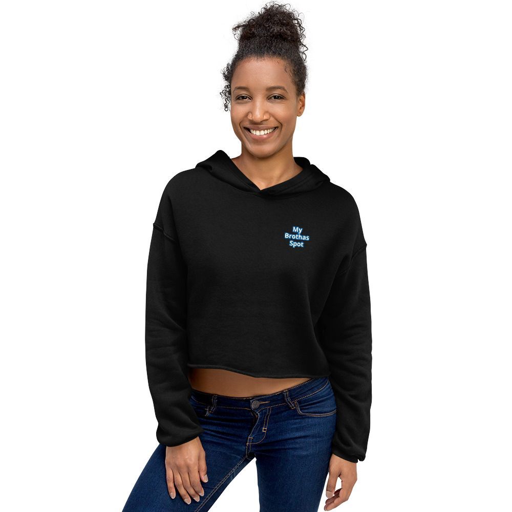 Person in a black cropped hoodie and blue jeans, smiling against a white background