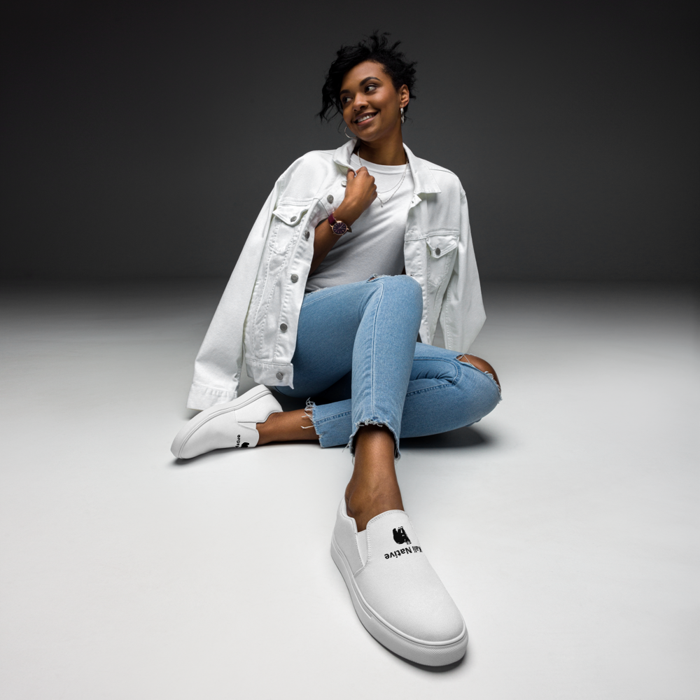 Woman in white jacket and jeans sitting on a gray studio floor, smiling at the camera.