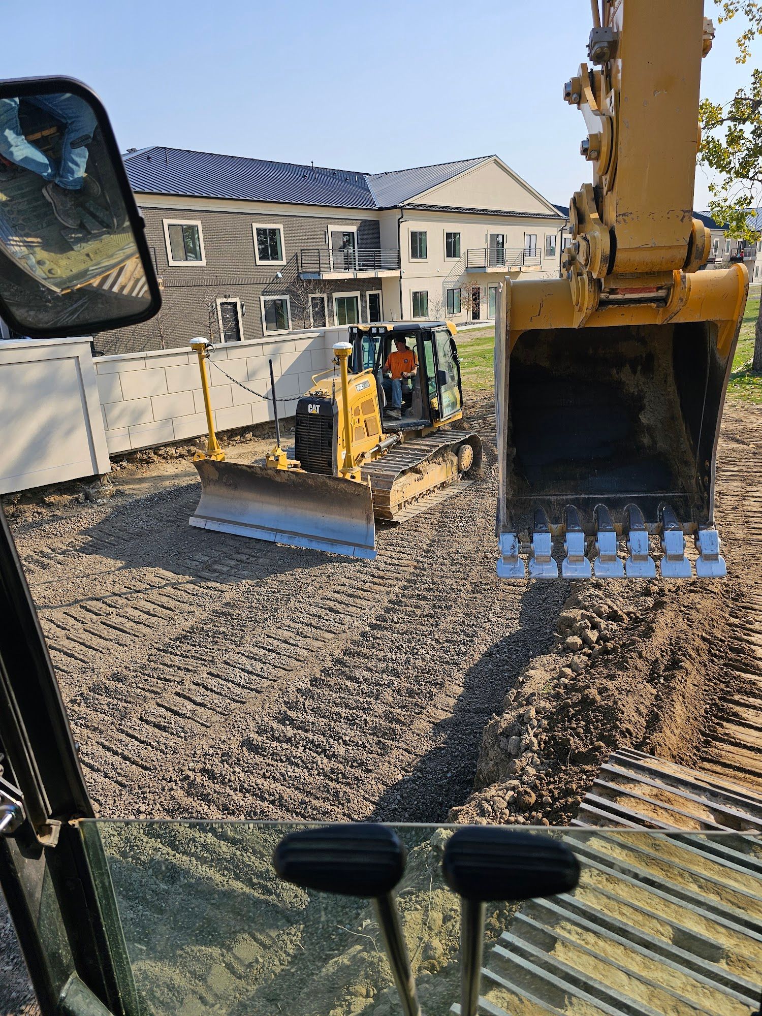 Construction site: excavator, bulldozer, and worker, with a building in the background.