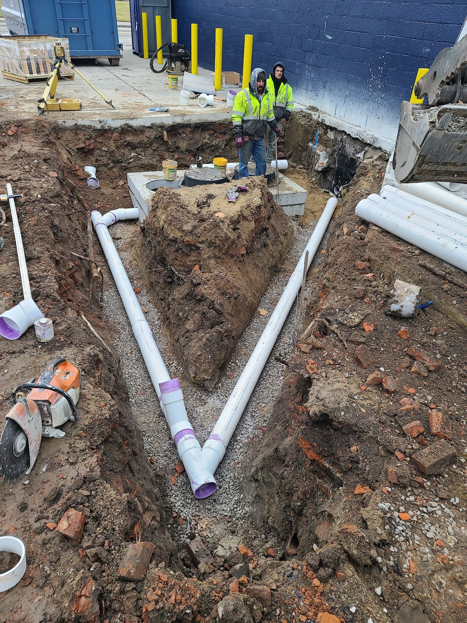 Construction workers install plumbing in a deep trench. White pipes form a 