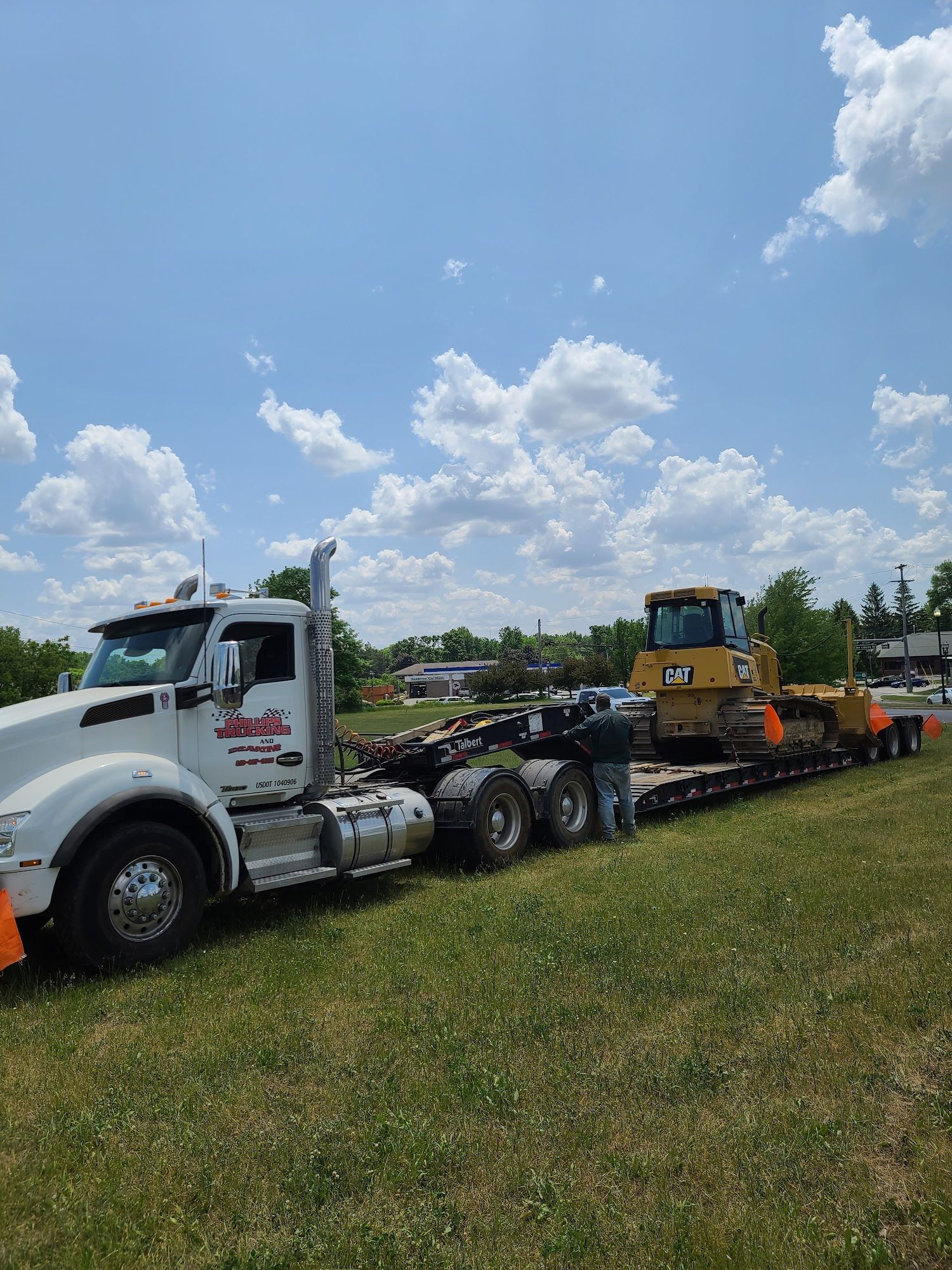 Truck transporting a yellow bulldozer on a flatbed trailer, parked on grass under a blue sky.