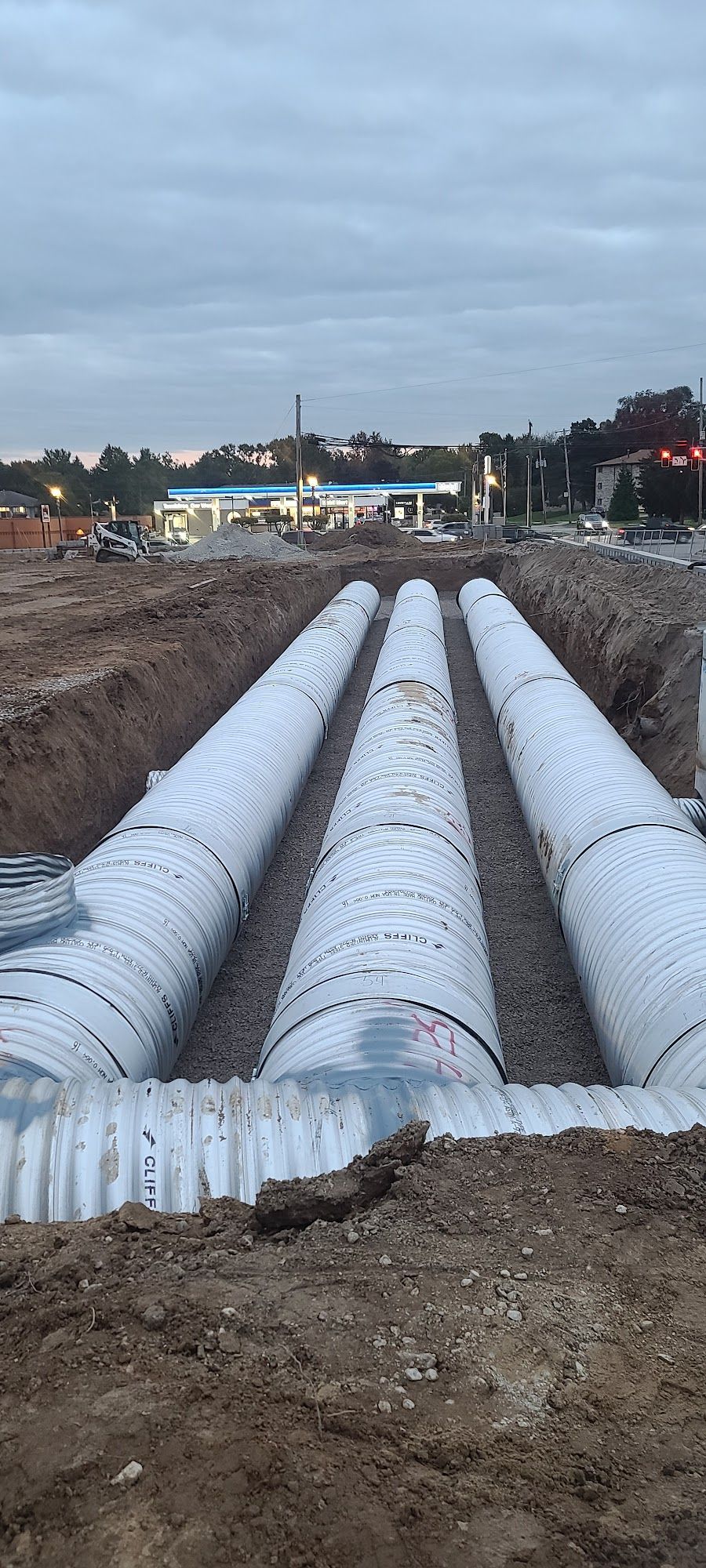 Three large pipes in an excavated trench, possibly for infrastructure work; d
