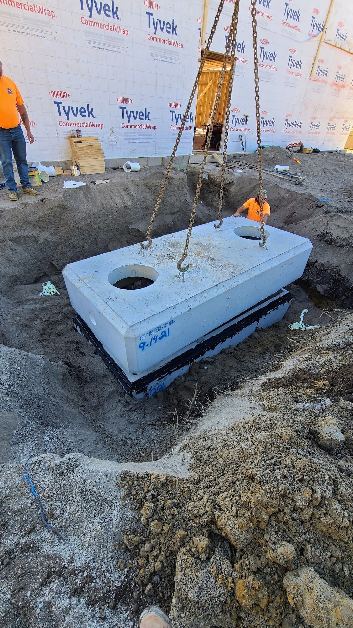 A concrete septic tank is lowered into a hole by a crane at a construction site.