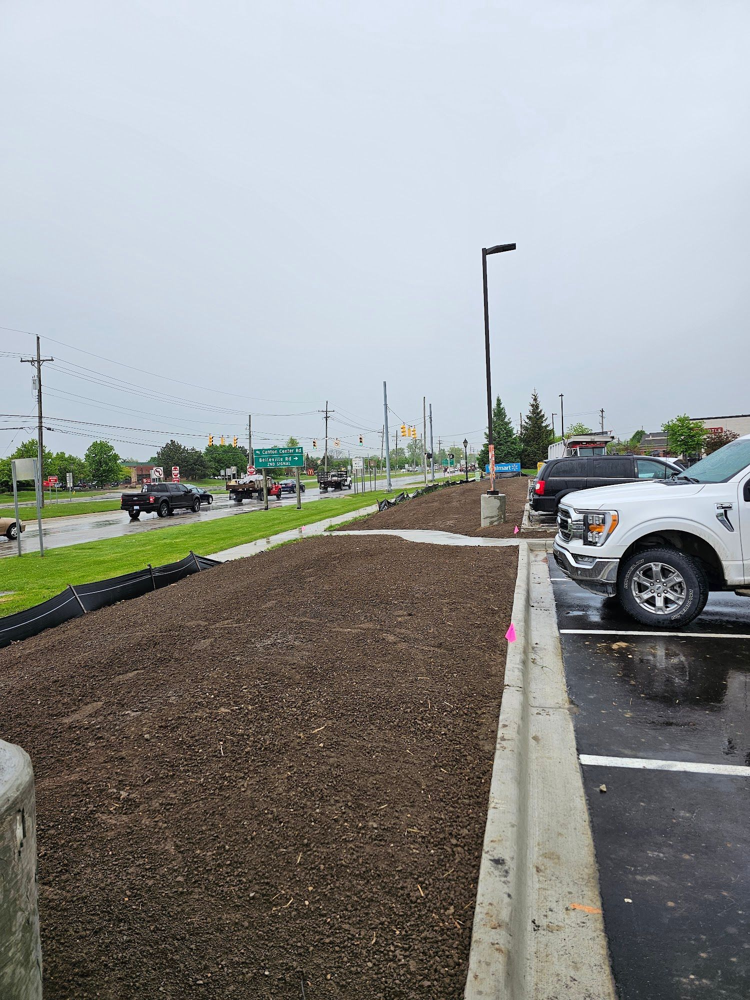 Landscaped area with brown mulch next to a parking lot and road. Overcast day.