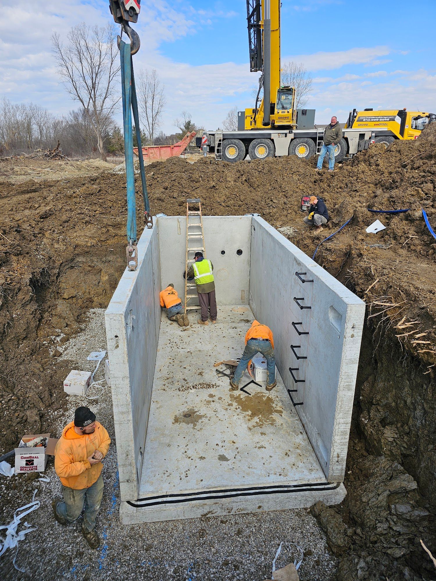 Construction workers in a rectangular concrete structure, suspended by a crane. 