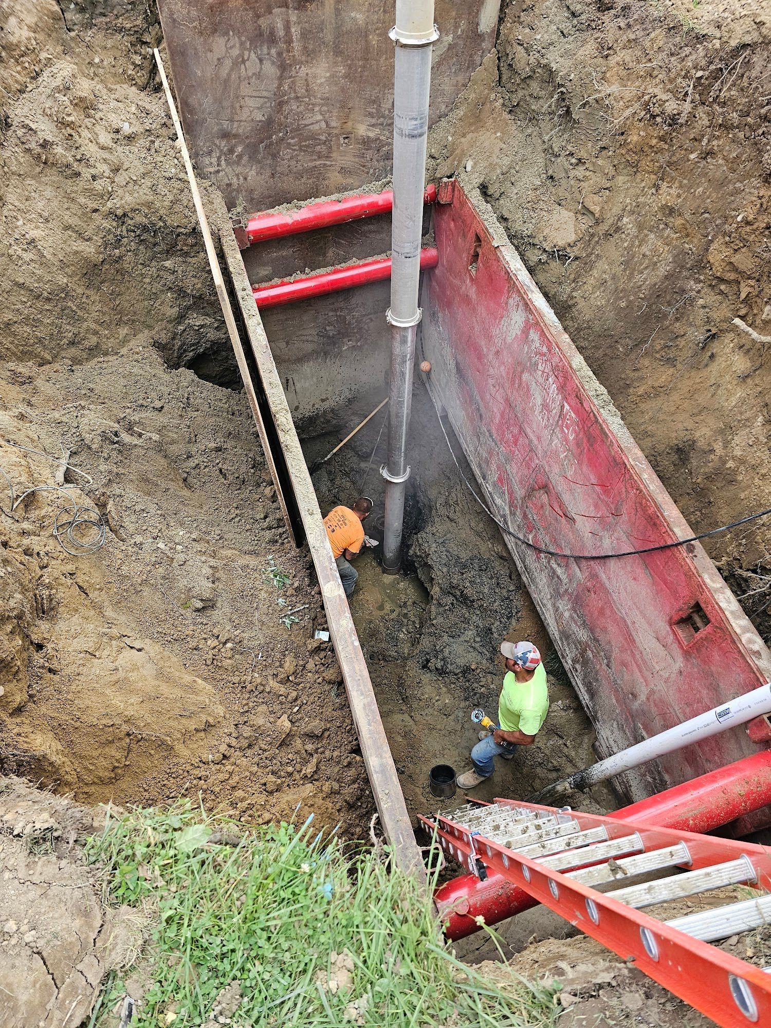 Trench with shoring, pipes, and worker; ladder, safety vest.