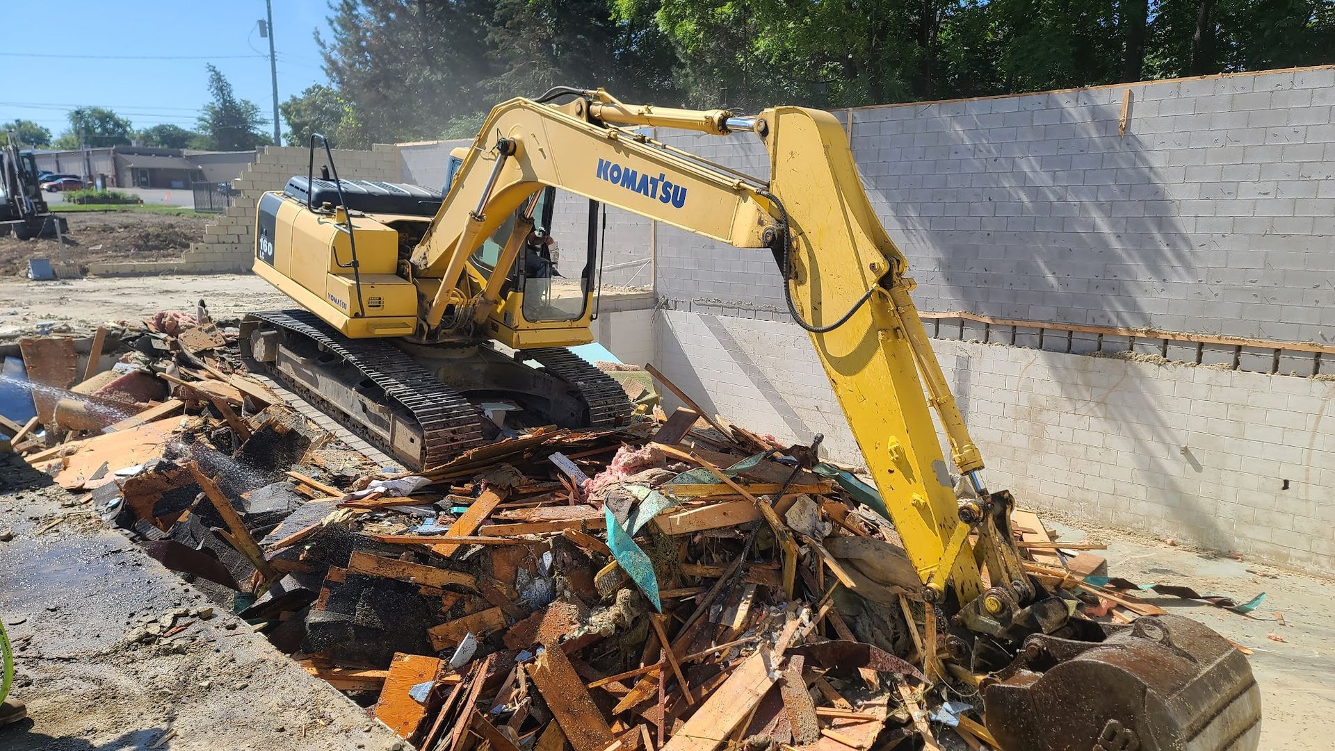 Yellow excavator demolishing debris in a construction site with a concrete wall in the background.