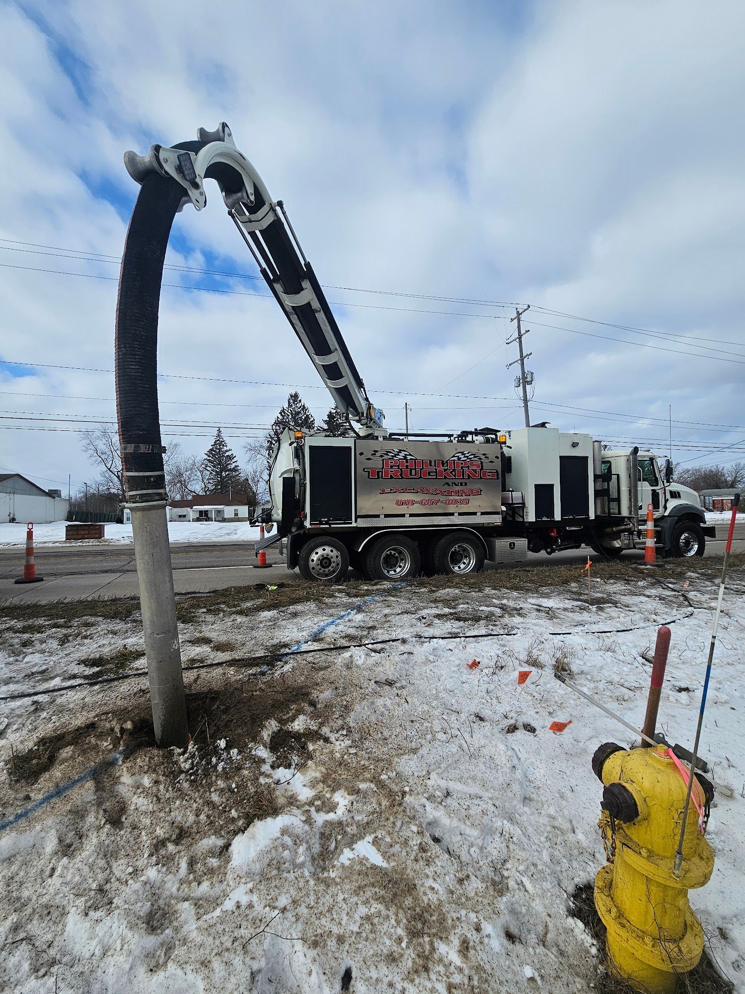 A white industrial truck with a long arm vacuuming a utility pole near a yellow fire hydrant in snow.
