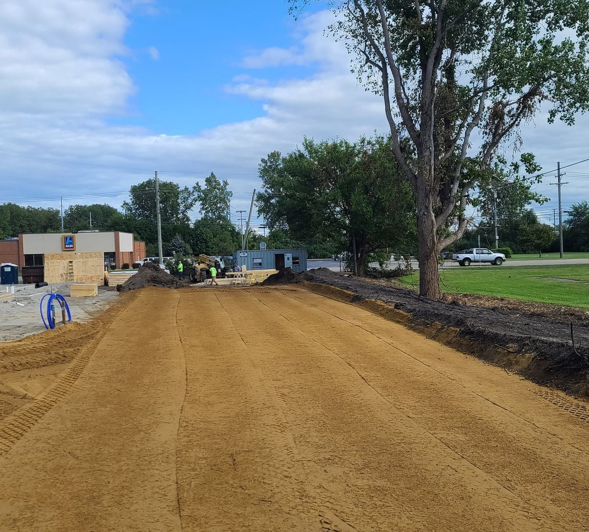 Dirt road construction site with trees, equipment, and a partly cloudy sky