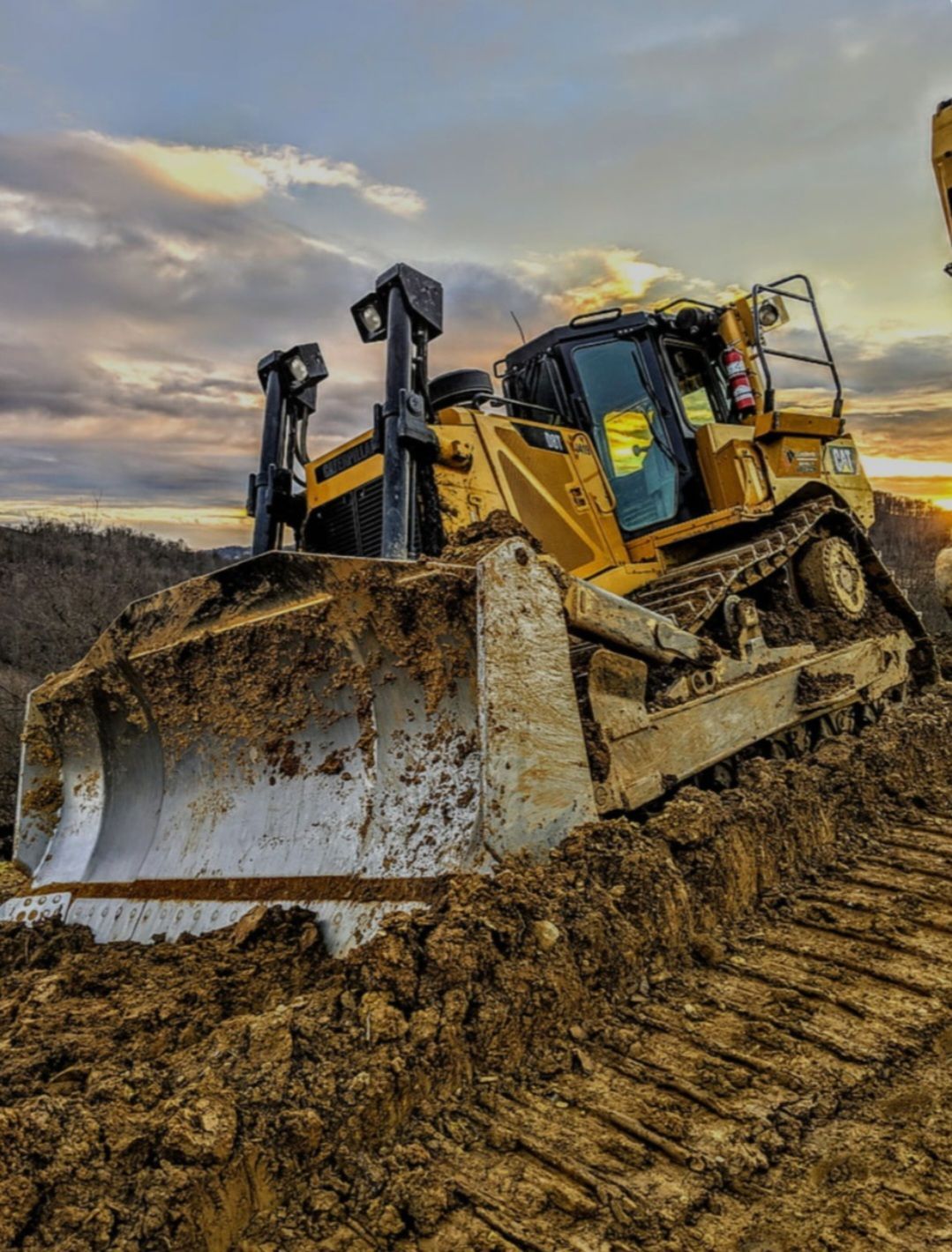 Yellow bulldozer on muddy ground with setting sun in background.