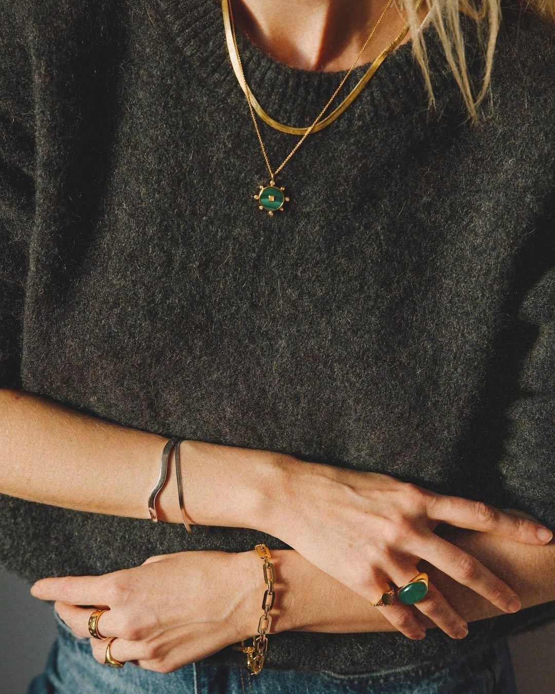 Femme portant des bijoux en or et un pull vert, avec des bracelets et une grande bague.