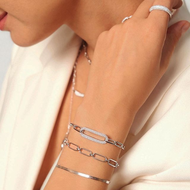 Femme portant plusieurs bracelets en argent et une bague, la main près du visage.