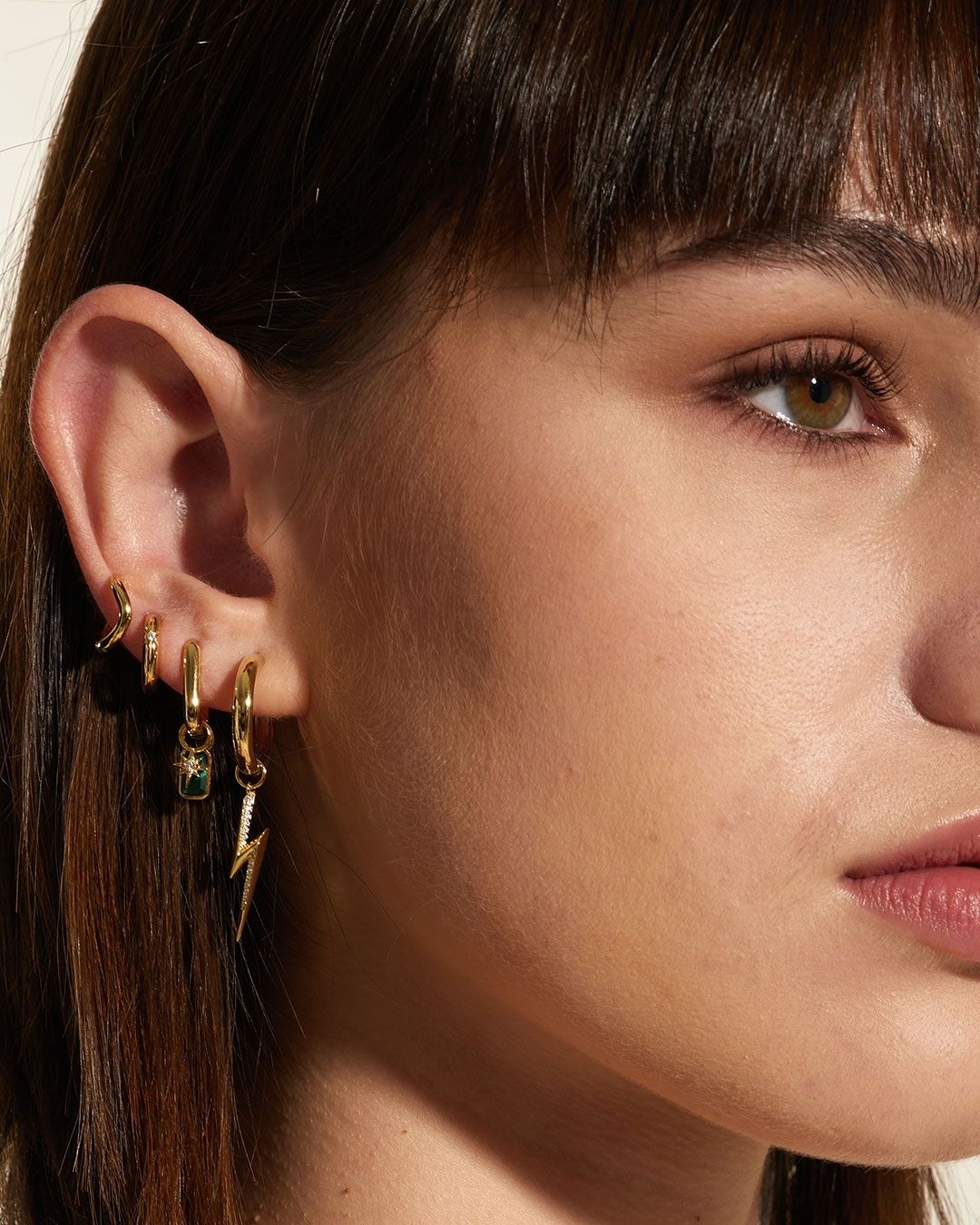 Femme avec plusieurs boucles d'oreilles créoles en or, dont un éclair et une pierre précieuse.