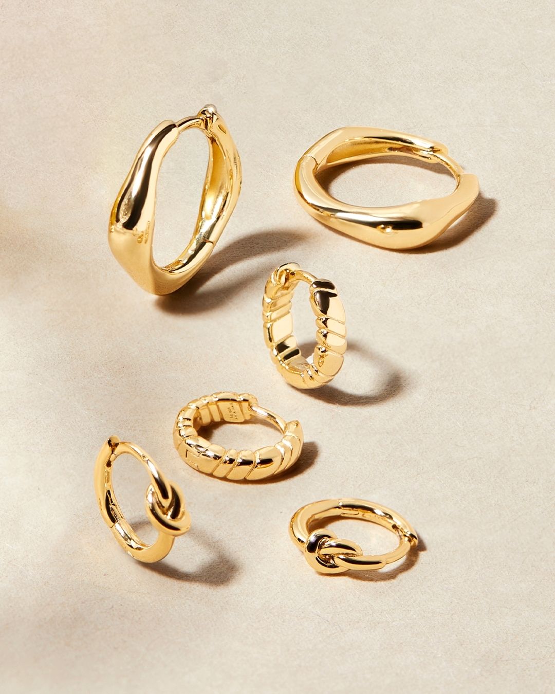 Boucles d'oreilles créoles dorées de différents styles disposées sur un fond neutre.
