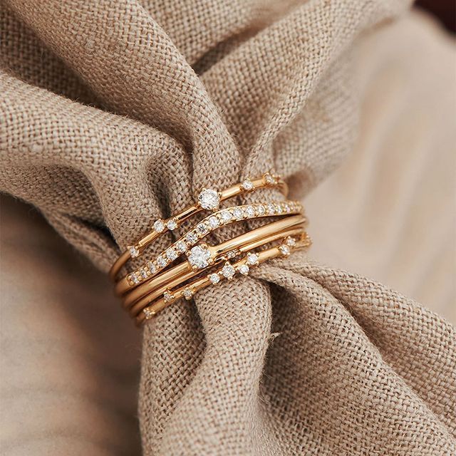 Pile de bagues en or avec diamants sur un tissu beige.