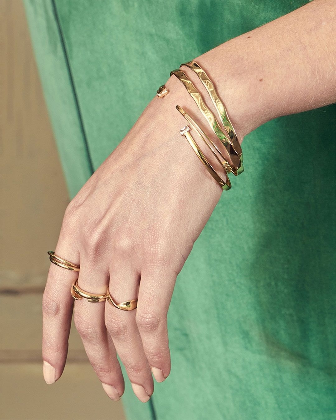 Main de femme portant des bracelets et des bagues en or, sur fond de robe verte.