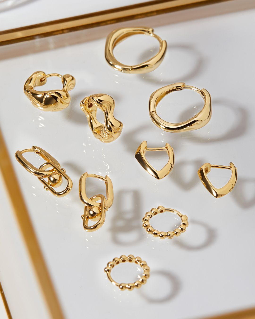 Boucles d'oreilles en or de différentes formes présentées sur une surface blanche.